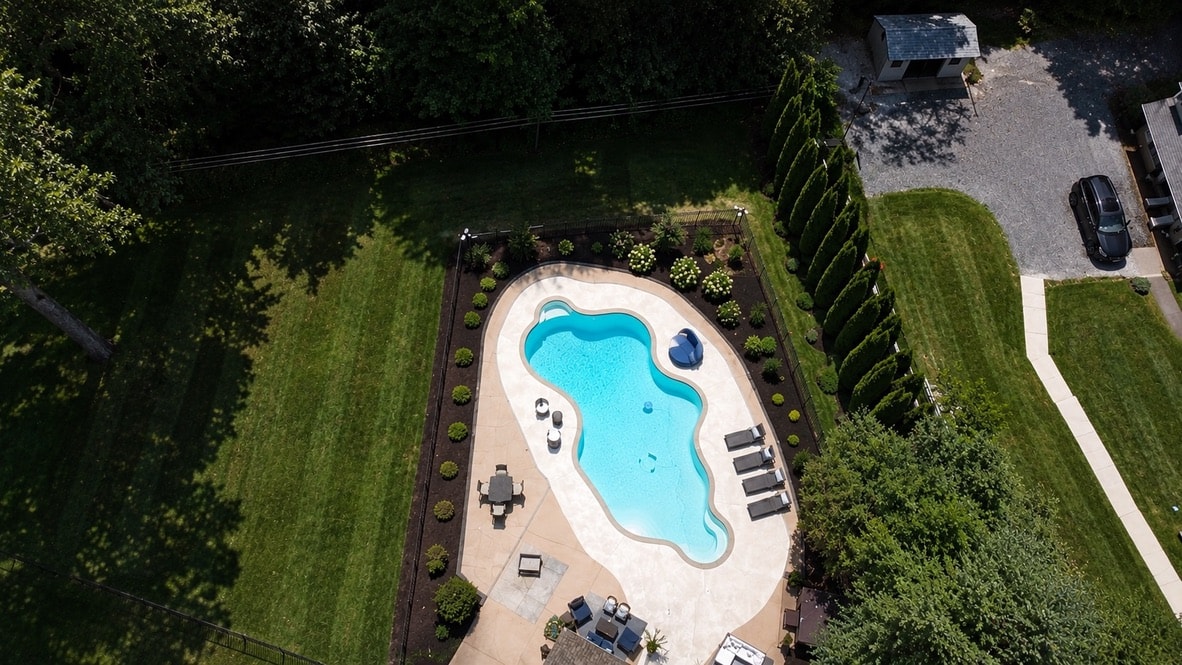Aerial view of a professionally landscaped backyard with a pool, layered planting beds, and mature screening trees
